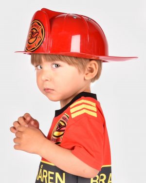Pojke som bär en röd brandmanshjälm fotograferad från sidan
