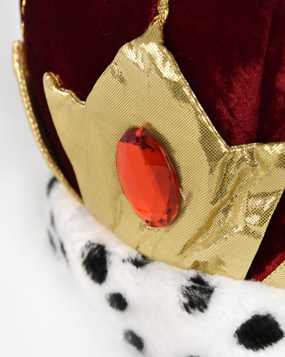 Närbild på framsidan av kungakrona. Kungakronan är sydd i röd sammet och har en svartvit kant i fuskpäls, guldiga detaljer samt en röd plexisten fram.