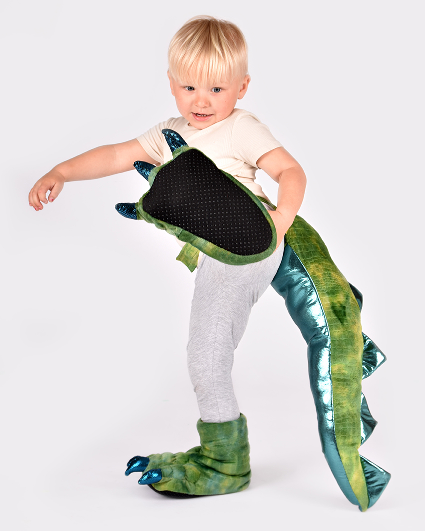 pojke sparkar mot kameran iklädd grön dinosauriesvans samt matchande mystofflor