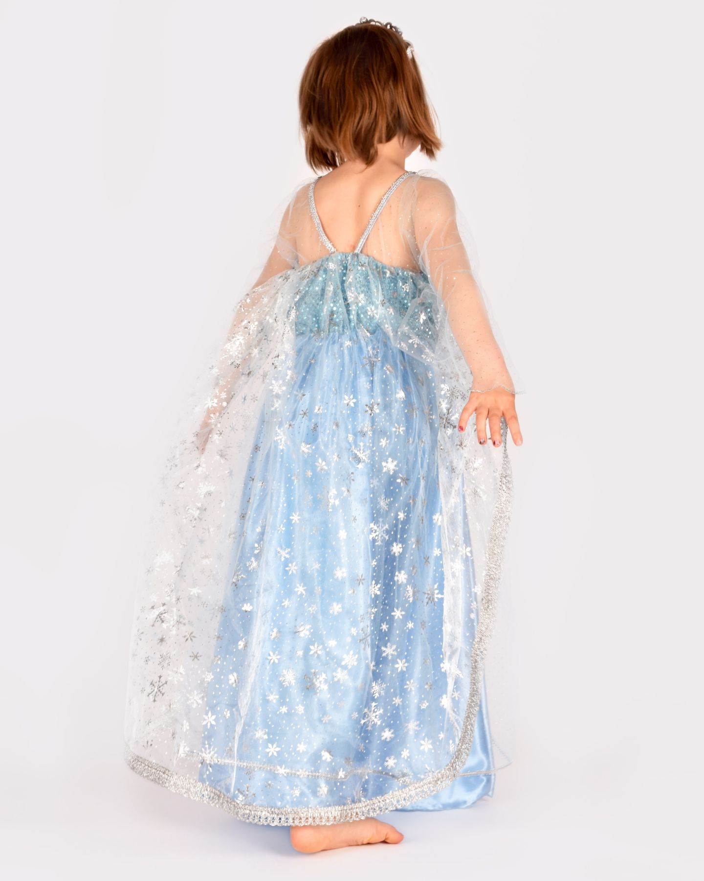 Flicka som bär en ljusblå Frost-inspirerad prinsessklänning. Flickan har ryggen vänd mot kameran, vilket visar det transparenta släpet med silvertryck föreställandes snöflingor.