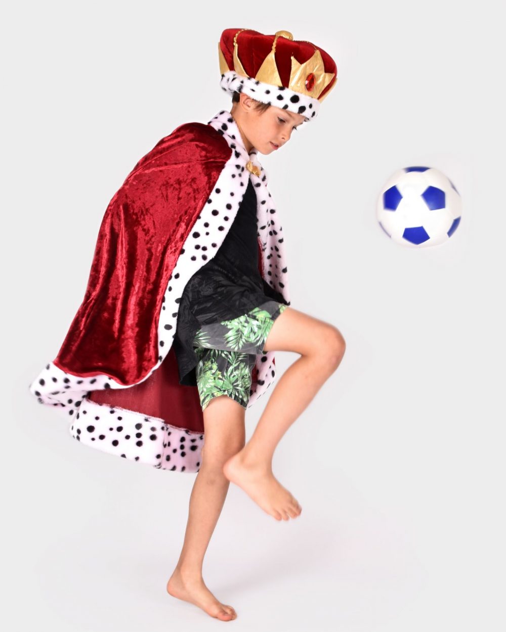 Pojke som spelar fotboll bär en en röd- och guldfärgad kungakrona, samt en röd kungacape. Båda plaggen har detaljer i svartvit fuskpäls.