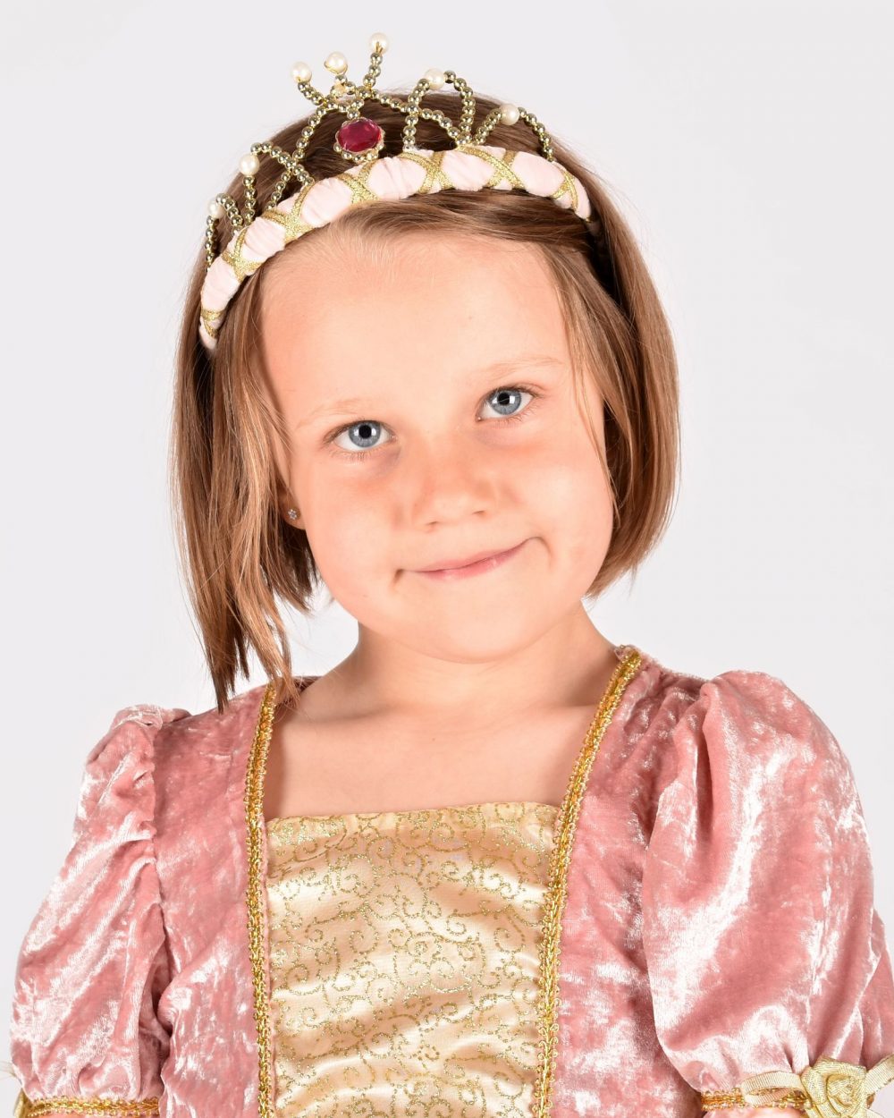 flicka bär sammetsklädd rosa prinsesstiara med guld- och pärldetaljer och rosa plexisten fram