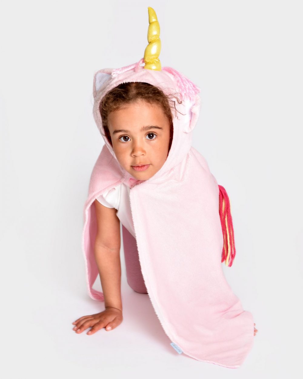 Flicka bär en rosa enhörningsdräkt med huva och en rosa prinsessklänning. Enhörningsdräkten har ett gyllene horn, två öron samt regnbågsfärgad man och svans.