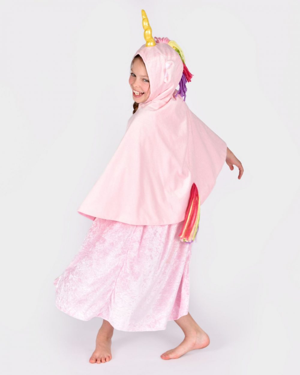 Flicka bär en rosa enhörningsdräkt med huva och en rosa prinsessklänning. Enhörningsdräkten har ett gyllene horn, två öron samt regnbågsfärgad man och svans.