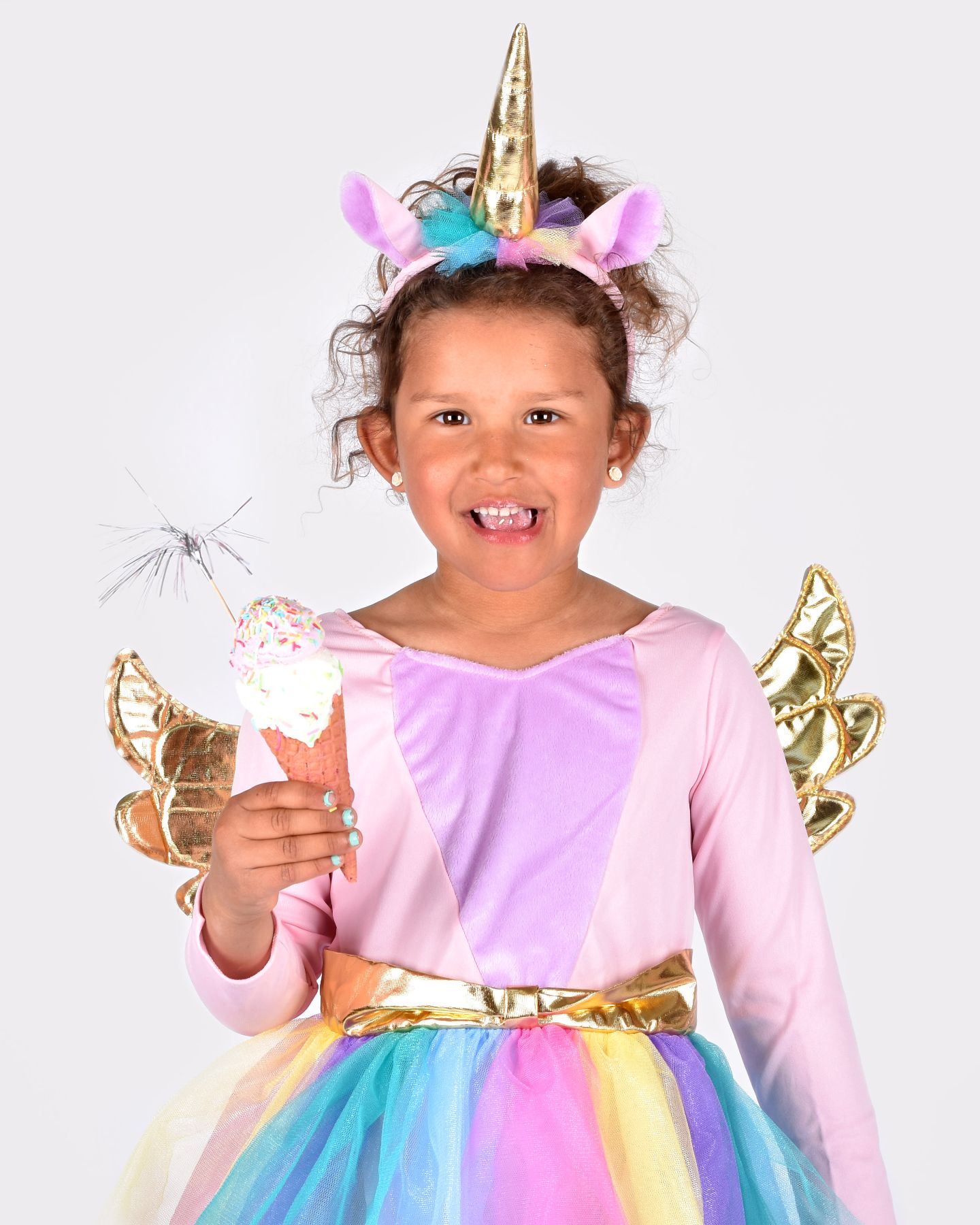 Barn som äter glass och bär en multifärgad enhörningsdräkt samt tillhörande diadem med guldigt spiralhorn.