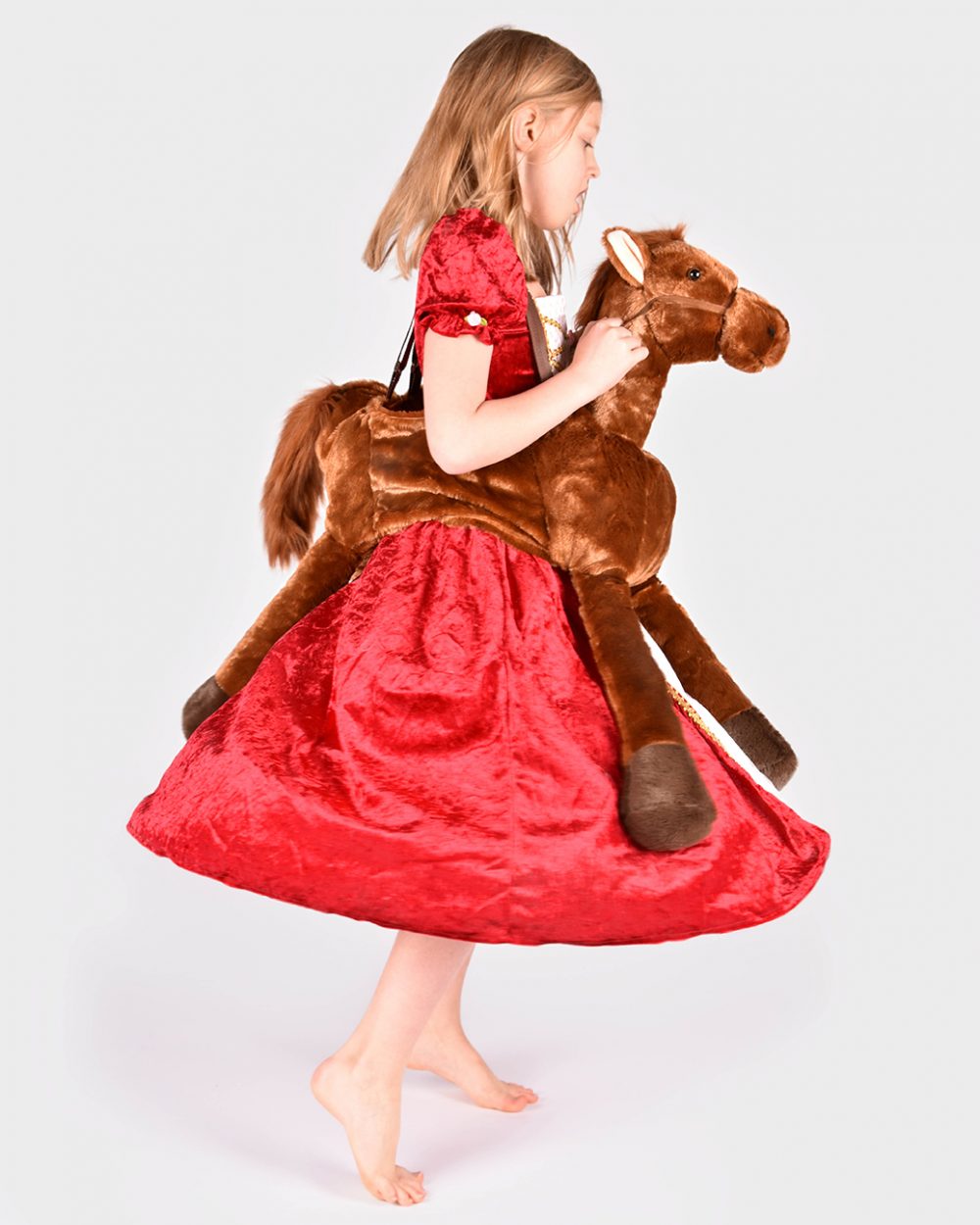flicka snurrar iklädd röd prinsessklänning och brun hästrideon